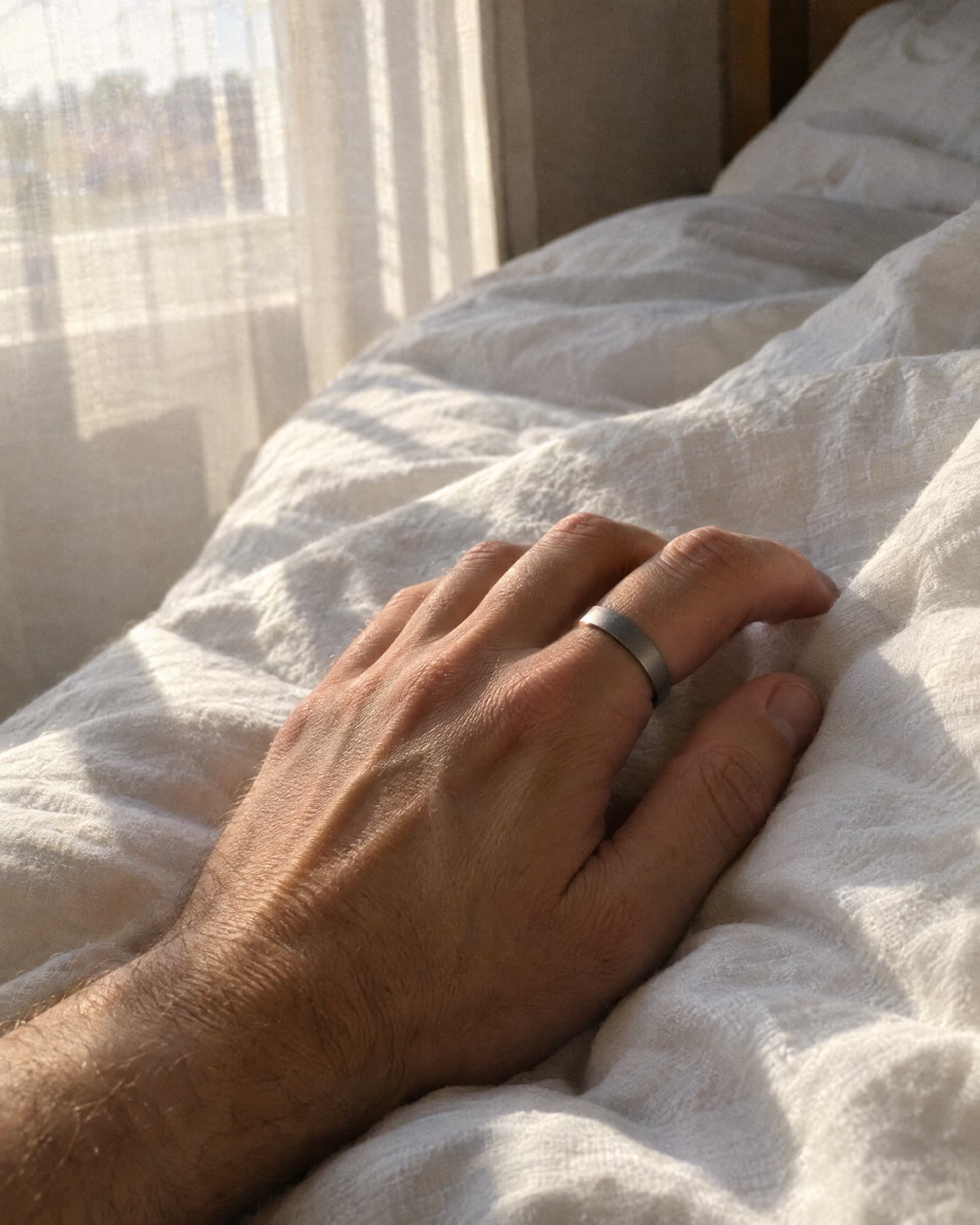 A relaxed hand wearing a plain smart ring, resting on linen sheets.